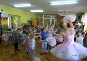Dzieci tańczą z baletnicą z rękoma uniesionymi w górę.